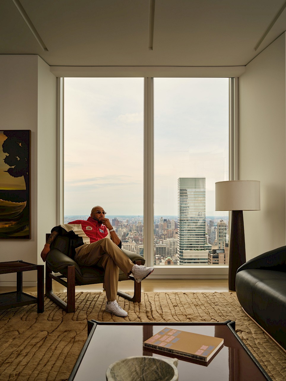 Swizz Beatz sits in a CB2 armchair by a floor-to-ceiling window overlooking a city skyline