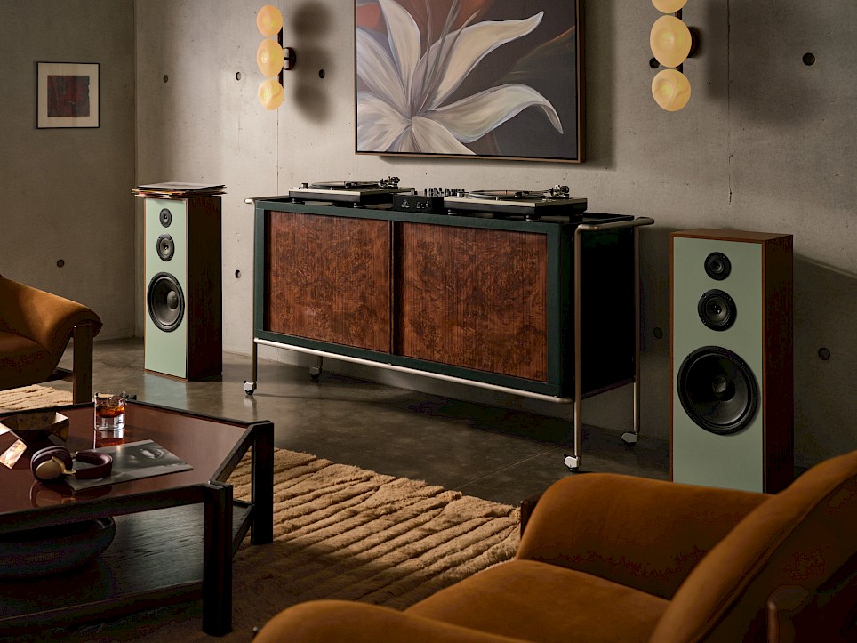 A Swizz Beatz CB2 retro-style media console on wheels with two turntables on top, flanked by two tall floor-standing speakers