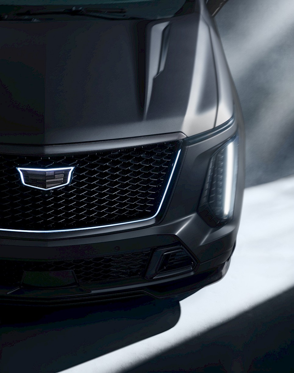Front view of a matte black Cadillac Escalade-V 125th Anniversary SUV with an illuminated grille emblem and vertical headlights