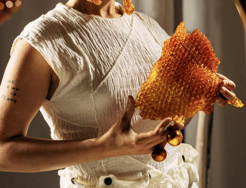 A person wearing a white top holds a large, translucent, amber-colored resin piece with a honeycomb-like texture